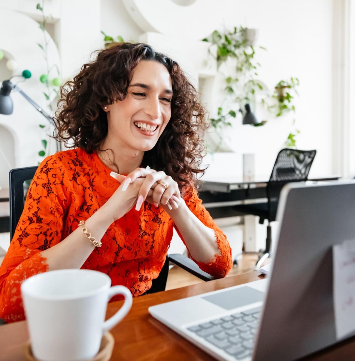 Woman at a desk smiles as she engages in a teleconference on her laptop.