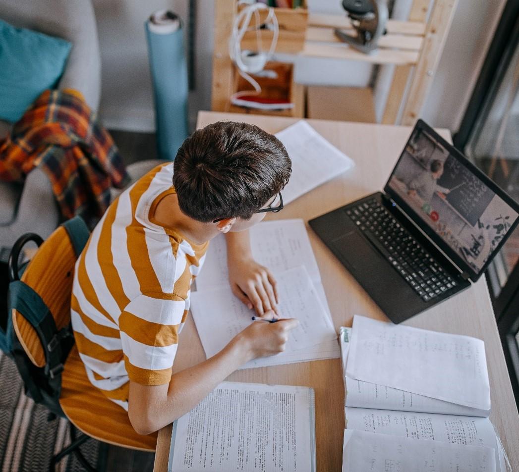 Teen boy concentrates with pen and paper in front of a STEM class conducted online.