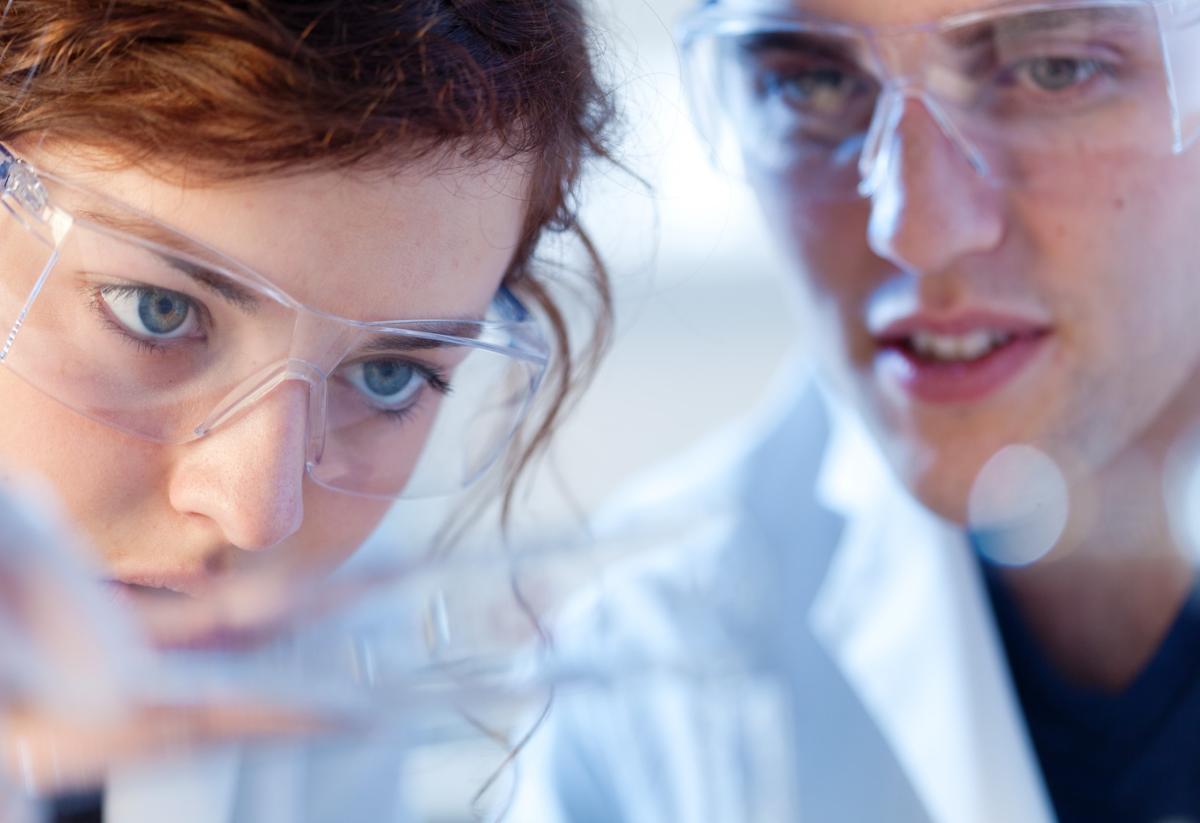 Two young scientists examine something not visible in the foreground.